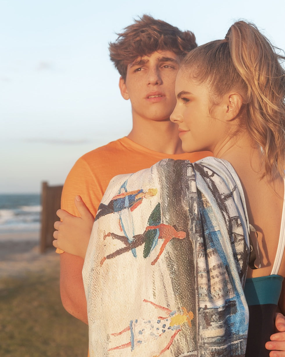 Models holding Surfers Paradise microfibre artistic towel. The towel shows an art inspiration of the Gold Coast’s suburb of Surfers Paradise. It includes at the beach the famous Surfers Paradise sign, the sea, lifeguards, yellow and red beach safety flag, lifeguard’s tower, surfers, families and kids, beach umbrellas and tall buildings at the back. Large size, 170cm x 95cm, soft touch, compact and sand free beach towel. An Aussie-inspired art showcasing magnificent landmarks and the Aussie lifestyle.