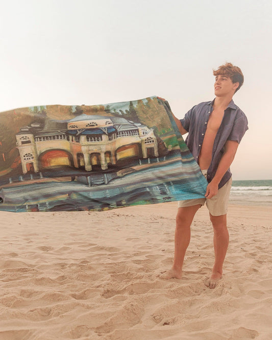 Male model holding Cottesloe Beach microfibre artistic towel. The towel shows the ocean, the Pavilion and trees behind it. Large size, 170cm x 95cm, soft touch, compact and sand free beach towel. An Aussie-inspired art showcasing magnificent landmarks and the Aussie lifestyle