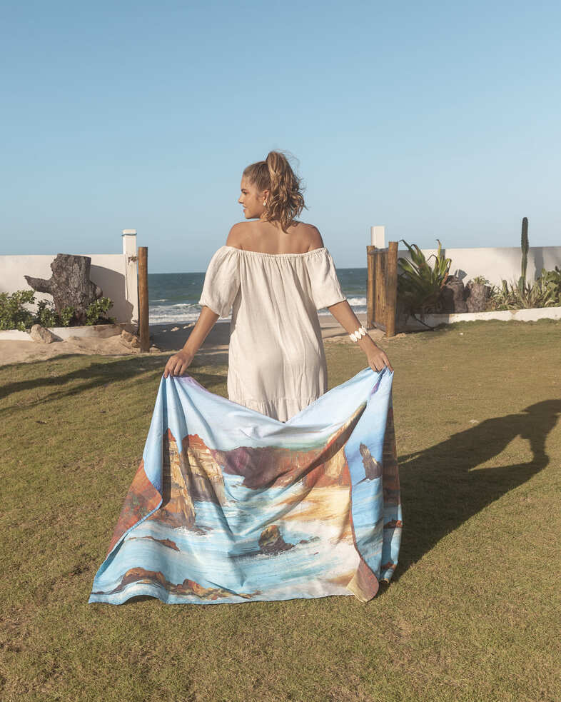 Female model with 12 Apostles microfibre artistic towel. The towel shows an art inspiration of Victoria’s magnificent twelve apostles. The art printed on the towel shows the cliffs, the rough ocean, and sunset sky. Large size, 170cm x 95cm, soft touch, compact and sand free beach towel. An Aussie-inspired art showcasing magnificent landmarks and the Aussie lifestyle.